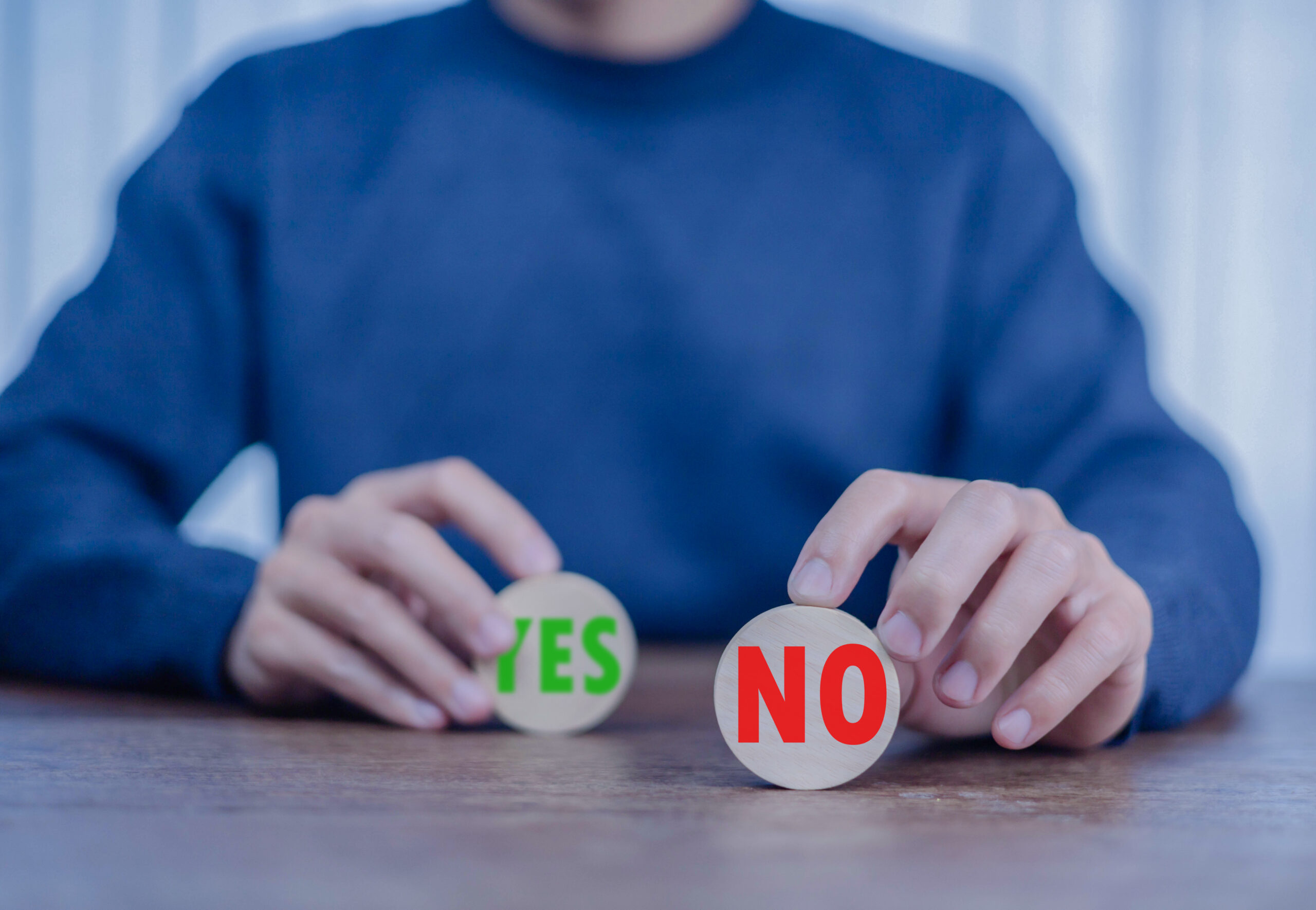 Business professional in blue shirt making decision between YES and NO wooden tokens on desk